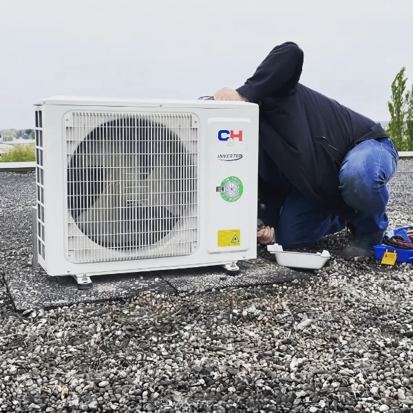 Techniker installiert die Aussenseinheit einer Klimaanlage auf einem Flachdach